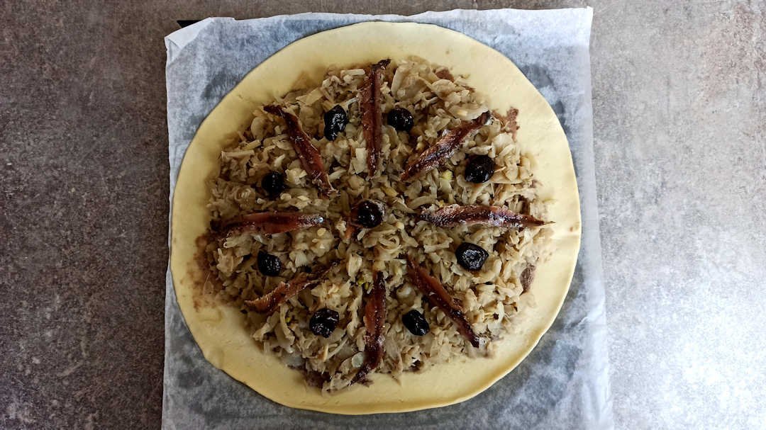 Décorer la pissaladière avec des filets d'anchois et des olives noires